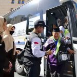 Petugas membantu jemaah turun dari bus.