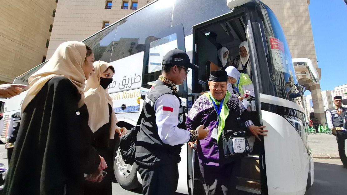 Petugas membantu jemaah turun dari bus.